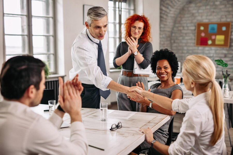 two-happy-business-people-shaking-hands-meeting-while-other-colleagues-are-applauding-them-office_637285-265